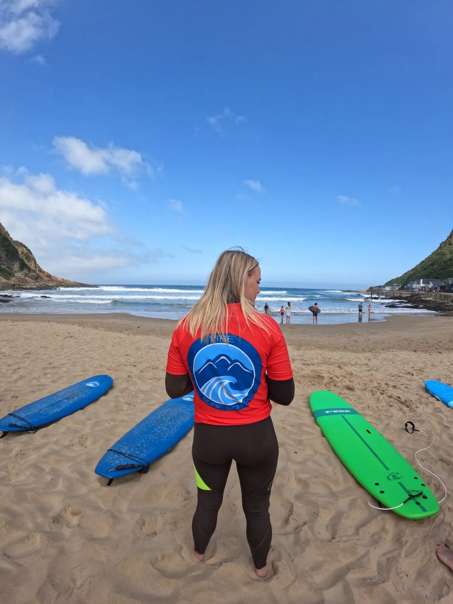 A student in a Vibe Surf School rash vest looking out at Herolds Bay